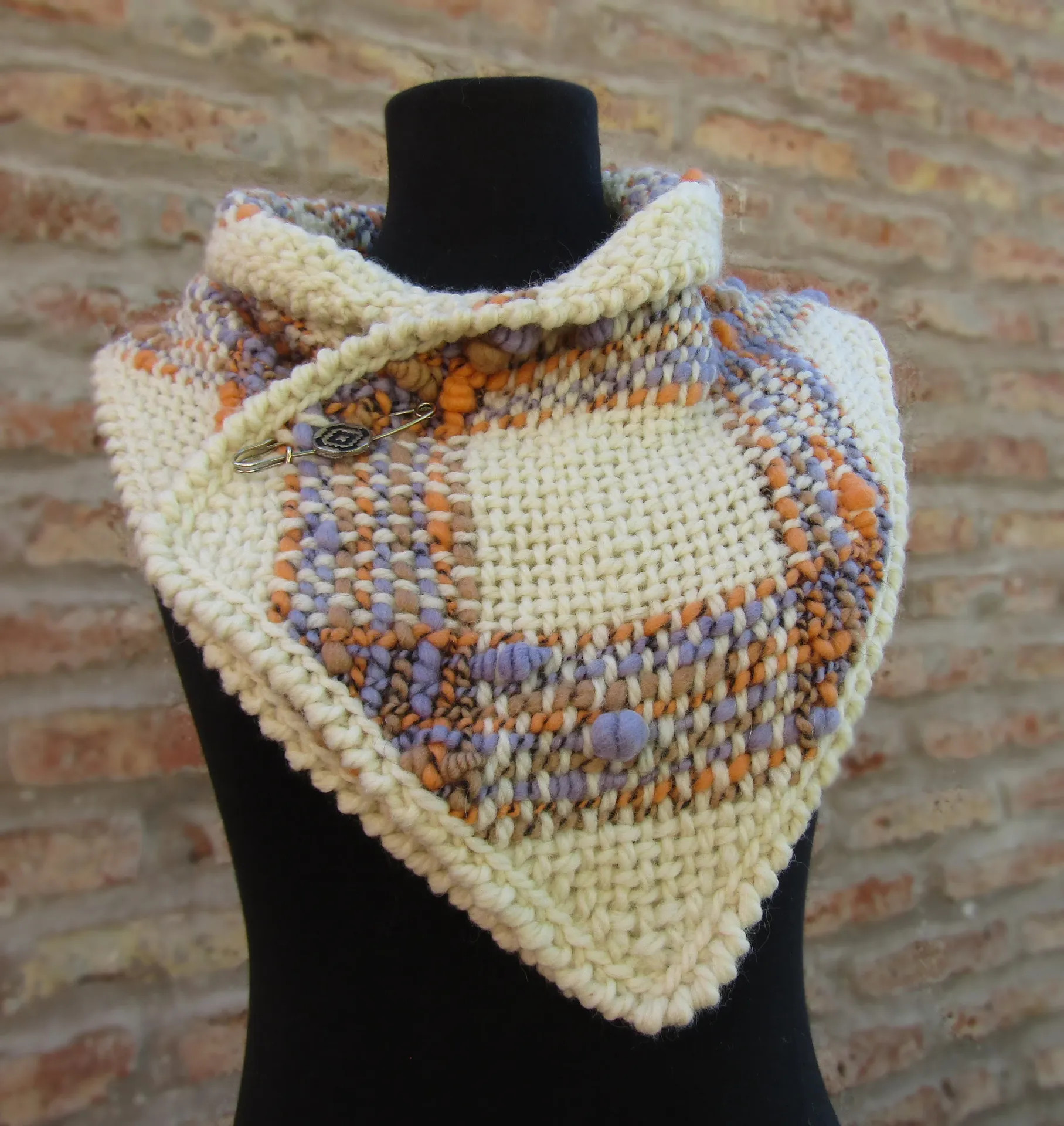 Handmade woven cowl scarf with multicolor pattern and cream chunky trim on a black mannequin.